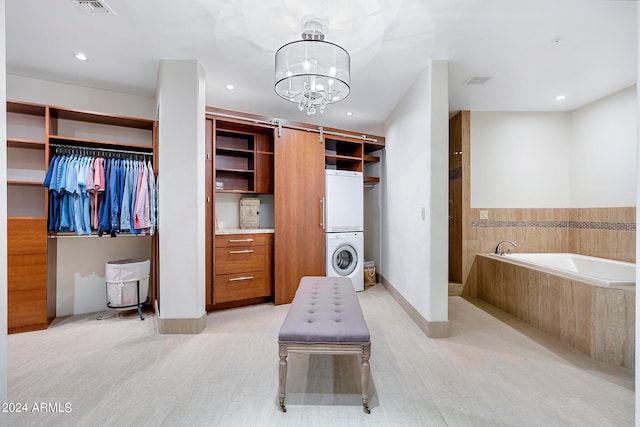 bathroom featuring tiled bath, a chandelier, and stacked washer / drying machine