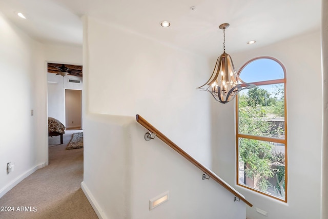 stairway with carpet floors and ceiling fan with notable chandelier