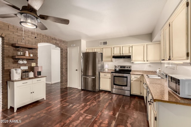 1676 W Sequoia Dr, Phoenix, AZ 85027 - kitchen with stainless steel appliances, ceiling fan, brick wall, dark wood-style floors, and cream cabinets