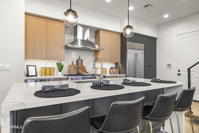 kitchen featuring decorative light fixtures, light wood-type flooring, stainless steel built in refrigerator, and wall chimney exhaust hood