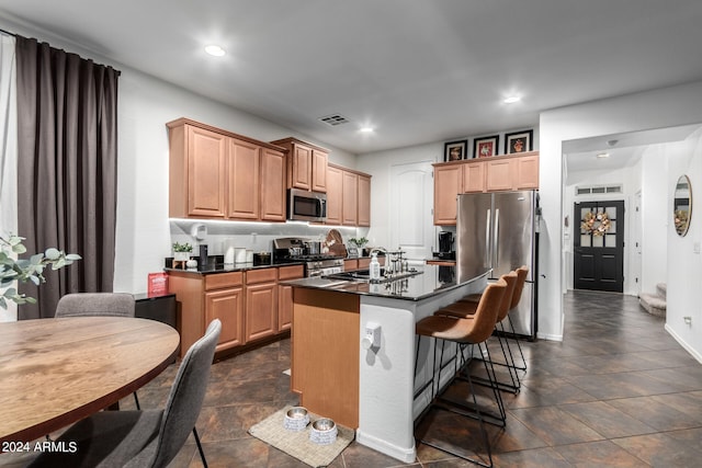 kitchen with a kitchen island with sink, sink, a kitchen bar, appliances with stainless steel finishes, and light brown cabinetry