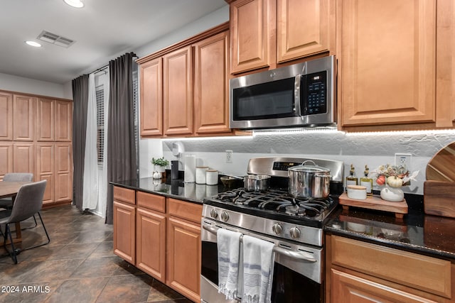 kitchen with dark tile patterned flooring, appliances with stainless steel finishes, and dark stone counters