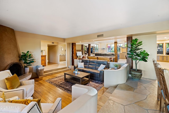 living area with a large fireplace, light wood-style flooring, and visible vents