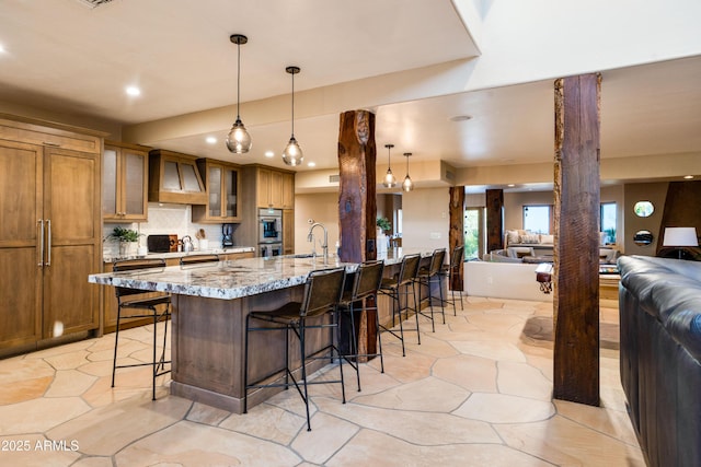 kitchen featuring a breakfast bar, brown cabinets, open floor plan, ornate columns, and premium range hood