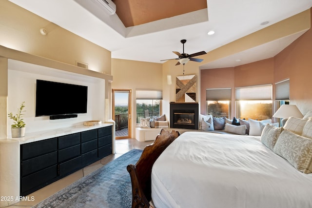 tiled bedroom with a glass covered fireplace, access to outside, a high ceiling, a tray ceiling, and recessed lighting