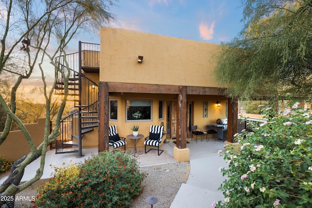 back of property at dusk with a patio area, stairs, and stucco siding