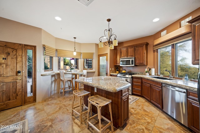 kitchen featuring light stone counters, decorative light fixtures, appliances with stainless steel finishes, a sink, and a kitchen island