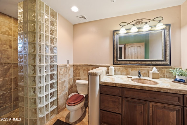 full bathroom featuring tile walls, visible vents, toilet, vanity, and a walk in shower