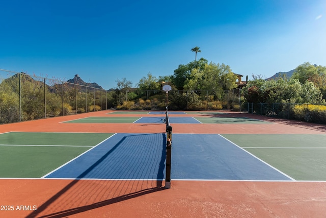 view of tennis court featuring community basketball court, a mountain view, and fence