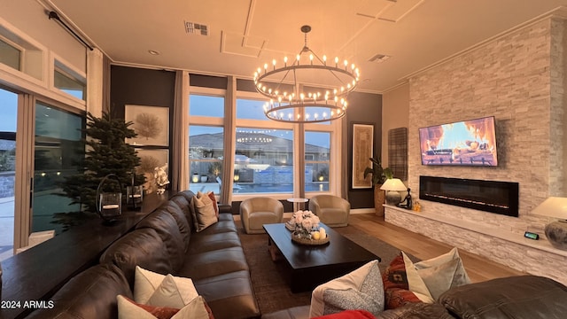 living room with crown molding, a fireplace, wood-type flooring, and an inviting chandelier