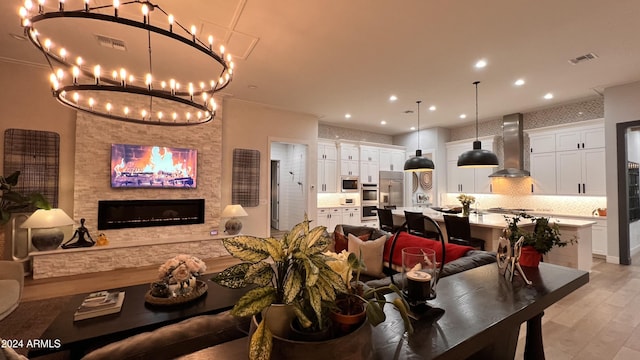 dining area with a fireplace, light hardwood / wood-style floors, an inviting chandelier, and crown molding