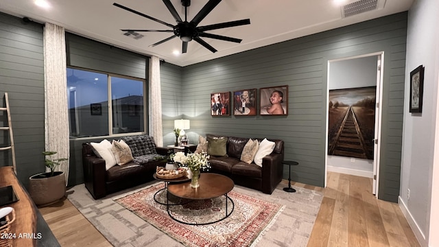 living room with light hardwood / wood-style flooring, ceiling fan, and wood walls