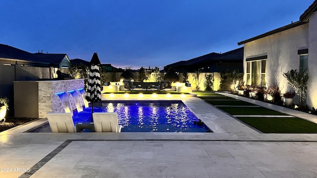 pool at dusk featuring a water view and a patio area