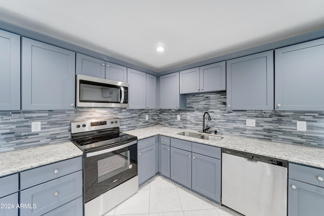 kitchen featuring sink, light stone counters, backsplash, light tile patterned floors, and appliances with stainless steel finishes