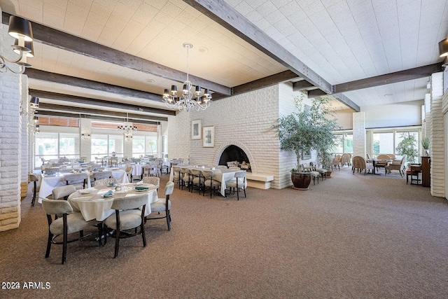 dining space featuring beamed ceiling, a chandelier, a brick fireplace, and a wealth of natural light