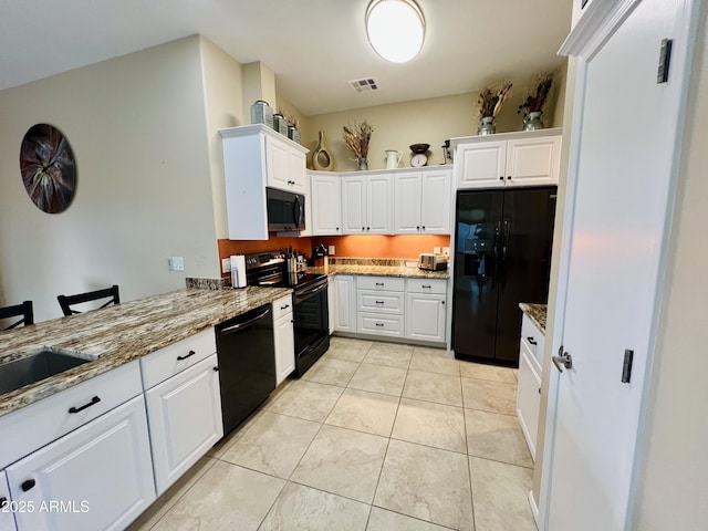 kitchen with stone counters, light tile patterned flooring, white cabinetry, a kitchen bar, and black appliances