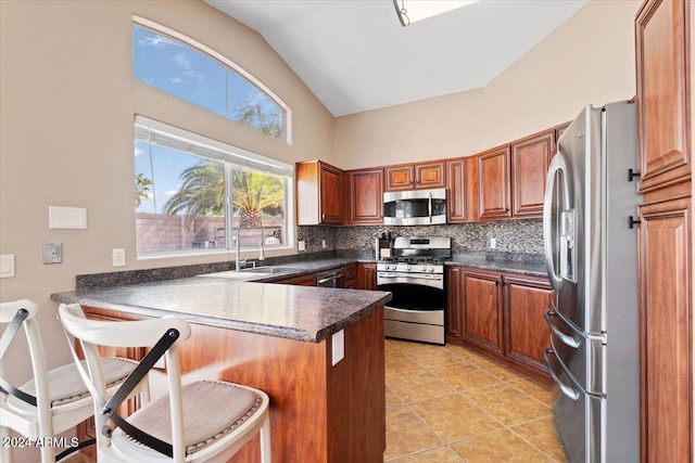 kitchen featuring appliances with stainless steel finishes, backsplash, kitchen peninsula, vaulted ceiling, and a breakfast bar area