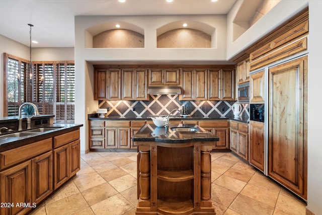 kitchen with stainless steel microwave, backsplash, sink, and a center island with sink