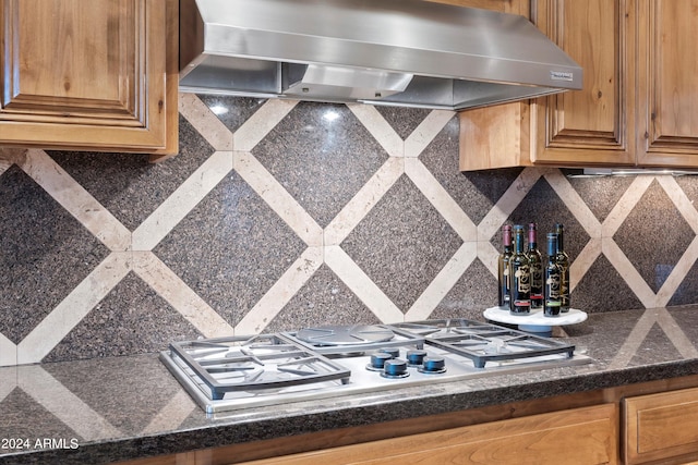 interior details featuring decorative backsplash, dark stone countertops, stainless steel gas stovetop, and range hood