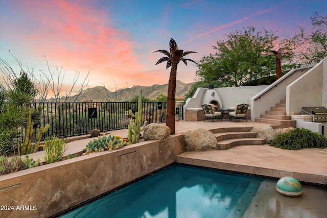 pool at dusk featuring a mountain view, a patio area, an outdoor kitchen, a grill, and outdoor lounge area