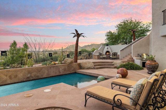 pool at dusk with a patio area, exterior fireplace, and area for grilling