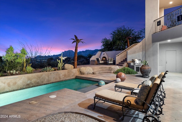 pool at dusk featuring a patio area and an outdoor fireplace