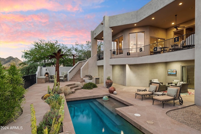 back house at dusk with a mountain view, ceiling fan, a fenced in pool, an outdoor living space, and a patio