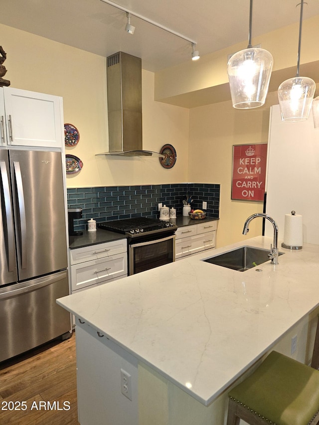 kitchen featuring dark stone counters, decorative backsplash, appliances with stainless steel finishes, wall chimney exhaust hood, and a sink