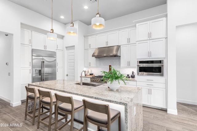 kitchen featuring appliances with stainless steel finishes, sink, decorative light fixtures, white cabinetry, and an island with sink