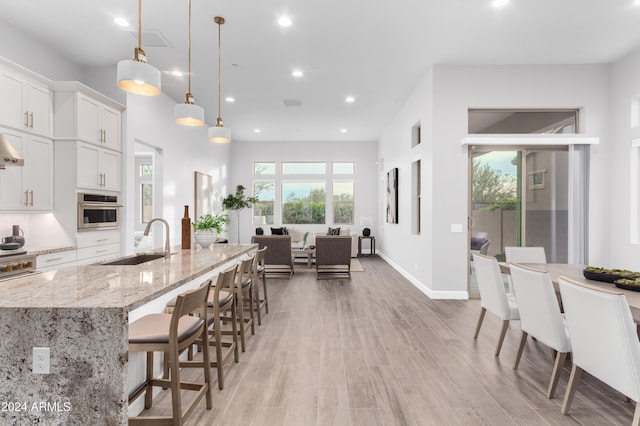 kitchen with pendant lighting, white cabinets, sink, light stone countertops, and a large island