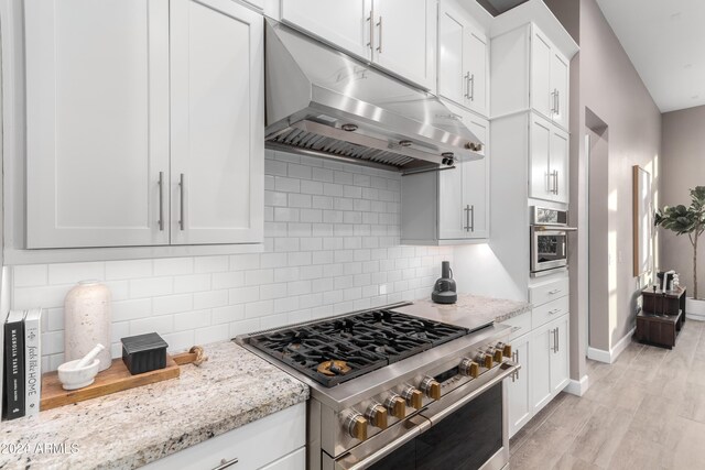 kitchen with light stone counters, light hardwood / wood-style floors, decorative backsplash, white cabinets, and appliances with stainless steel finishes