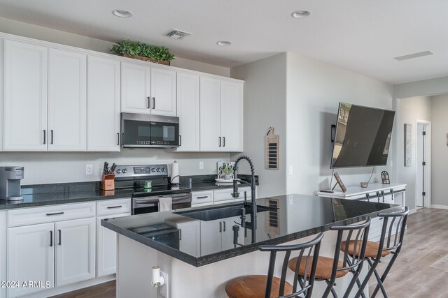 kitchen with sink, white cabinets, stainless steel appliances, and an island with sink