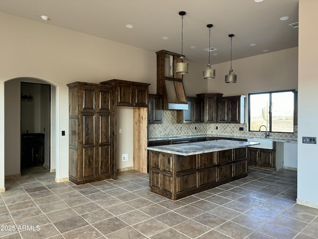 kitchen with a center island, arched walkways, dark brown cabinetry, a high ceiling, and decorative backsplash