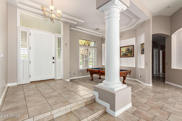 tiled foyer featuring a tray ceiling, an inviting chandelier, billiards, crown molding, and ornate columns