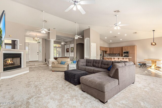 living room with light colored carpet, ceiling fan with notable chandelier, sink, and high vaulted ceiling