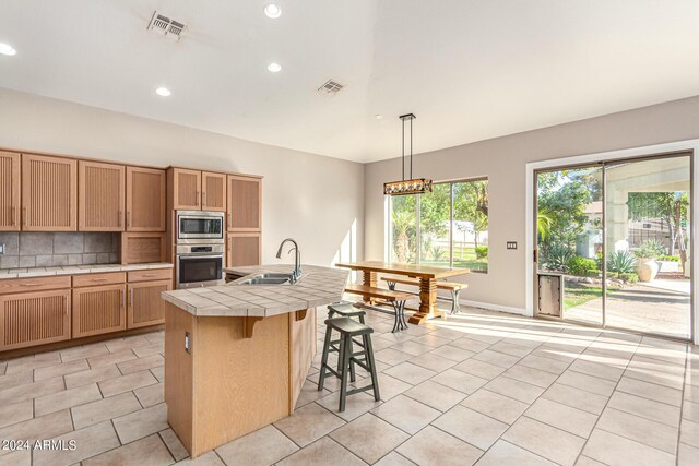 kitchen with appliances with stainless steel finishes, a kitchen breakfast bar, an island with sink, pendant lighting, and sink