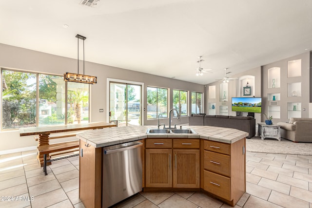 kitchen featuring ceiling fan, an island with sink, sink, stainless steel dishwasher, and tile countertops