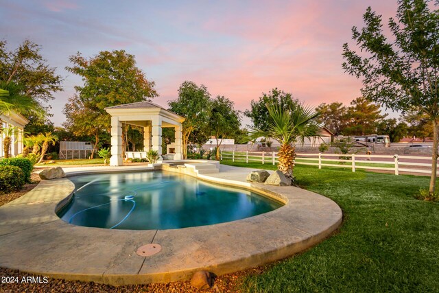 pool at dusk featuring a patio area and a yard