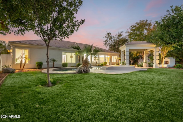 back house at dusk with a patio, a lawn, and a hot tub