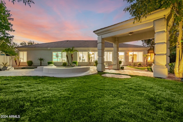 back house at dusk with a patio and a yard