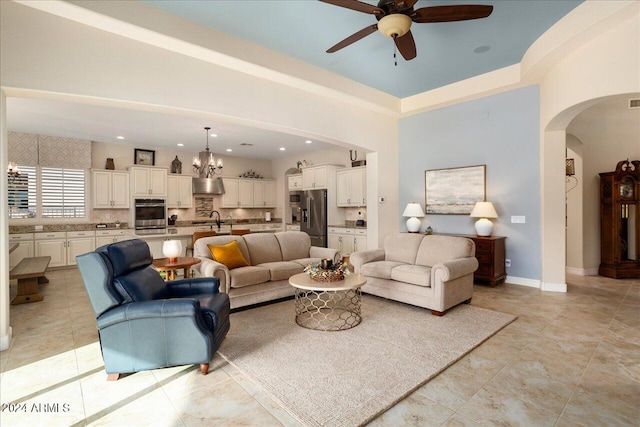 tiled living room with a high ceiling, sink, and ceiling fan with notable chandelier