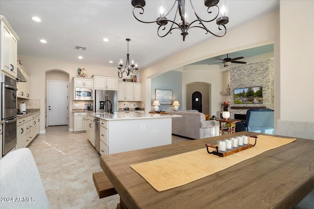 kitchen with ceiling fan, pendant lighting, a fireplace, an island with sink, and appliances with stainless steel finishes