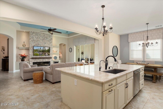 kitchen featuring cream cabinets, a kitchen island with sink, a large fireplace, sink, and light stone countertops