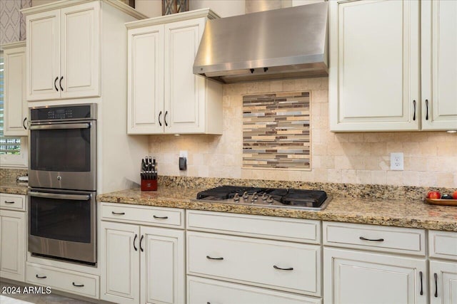 kitchen featuring light stone countertops, wall chimney exhaust hood, stainless steel appliances, and decorative backsplash