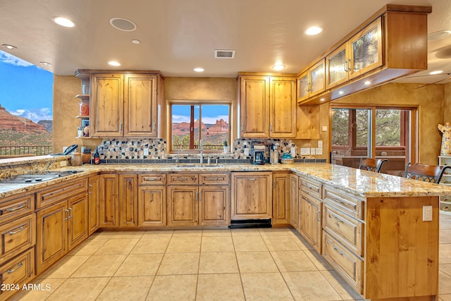 kitchen with a wealth of natural light, light stone countertops, kitchen peninsula, and sink