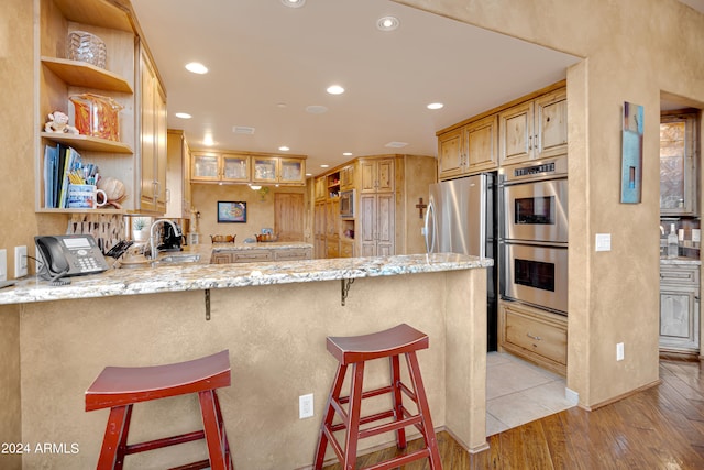 kitchen featuring sink, appliances with stainless steel finishes, kitchen peninsula, a breakfast bar area, and light hardwood / wood-style flooring