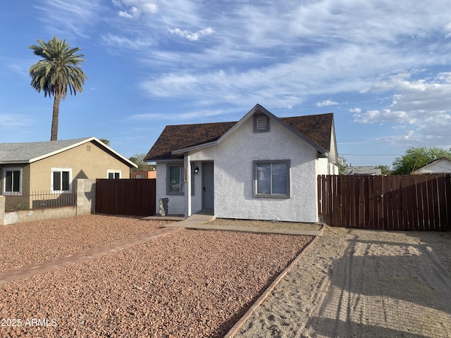 bungalow-style home with stucco siding, a shingled roof, and fence