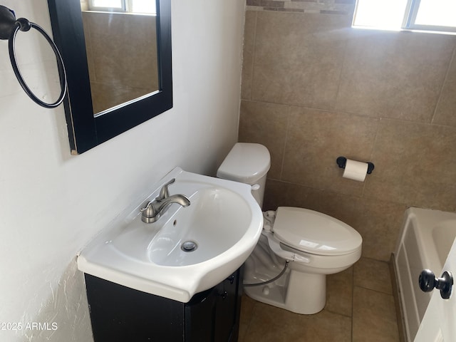 full bath with toilet, a tub to relax in, tile patterned flooring, vanity, and tile walls