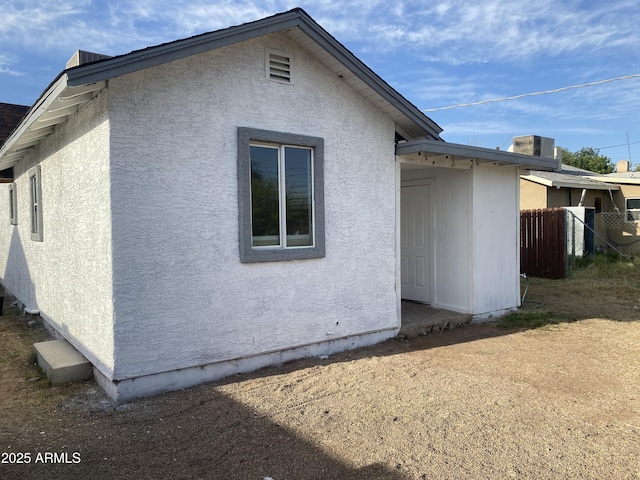 rear view of house with stucco siding and fence