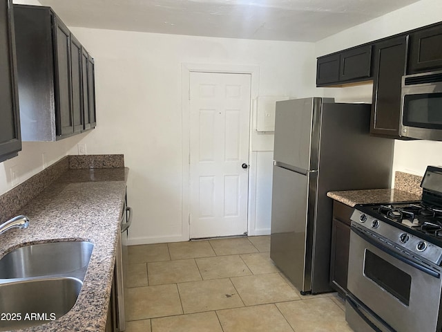 kitchen featuring appliances with stainless steel finishes, a sink, light tile patterned floors, dark stone counters, and baseboards